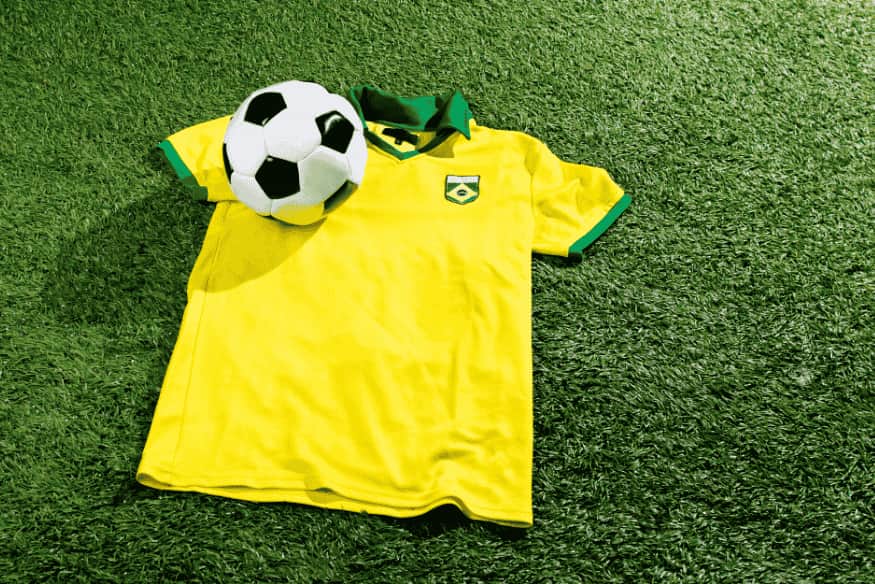 Camisa da seleção brasileira com bola de futebol sobre gramado.