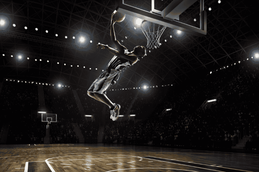 Jogador de basquete faz enterrada poderosa durante partida oficial em quadra iluminada.