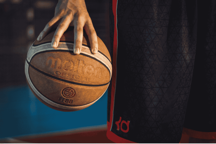 Jogador segurando bola de basquete oficial da Molten em quadra esportiva.