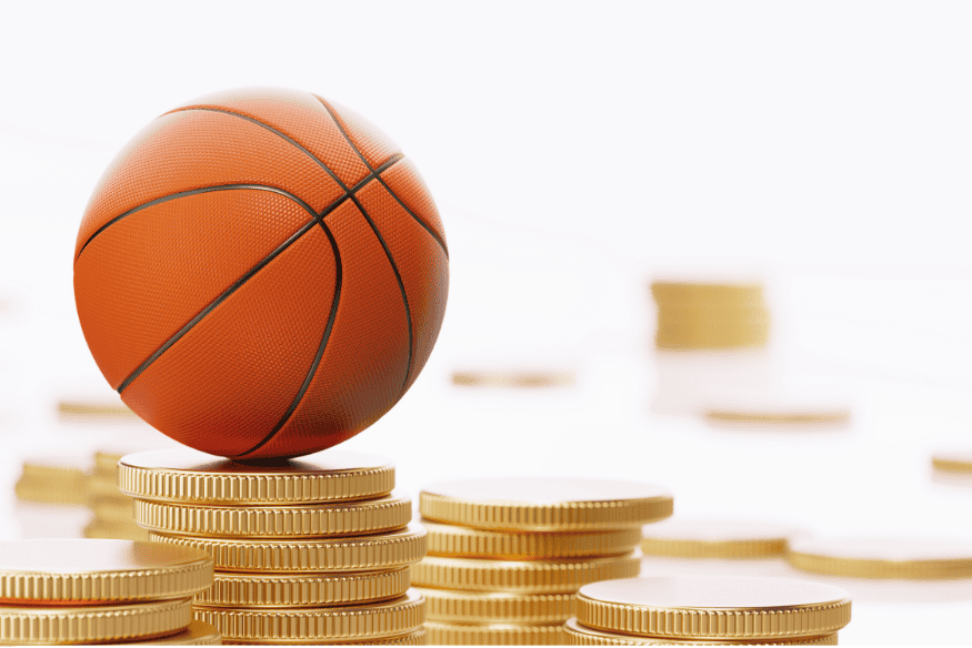 Bola de basquete sobre pilhas de moedas douradas em fundo claro.