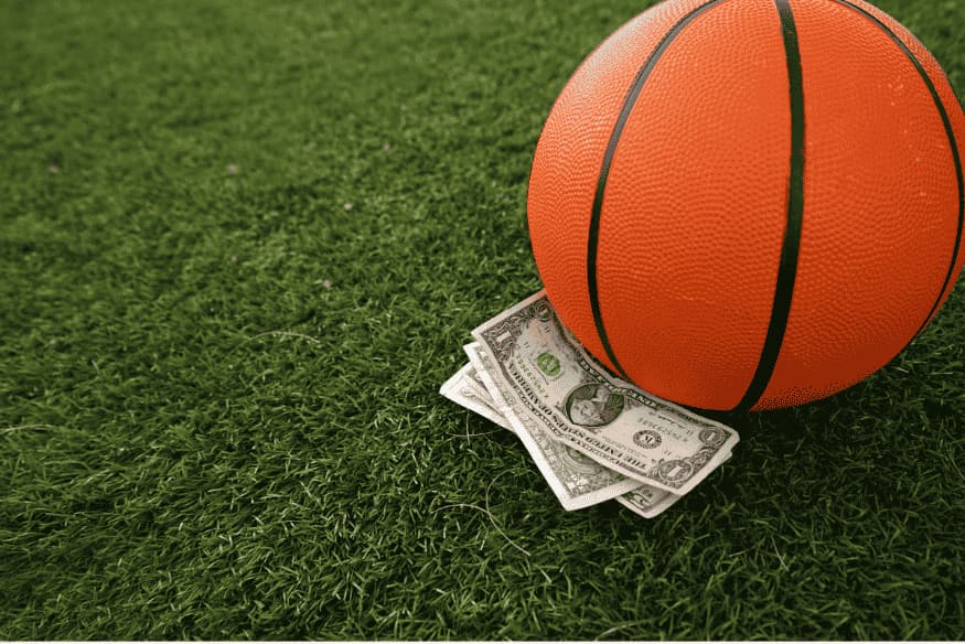 Bola de basquete sobre grama artificial com cédulas de dólar embaixo.