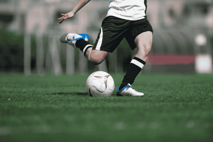 Jogador de futebol com uniforme preto e branco prestes a chutar uma bola em campo.
