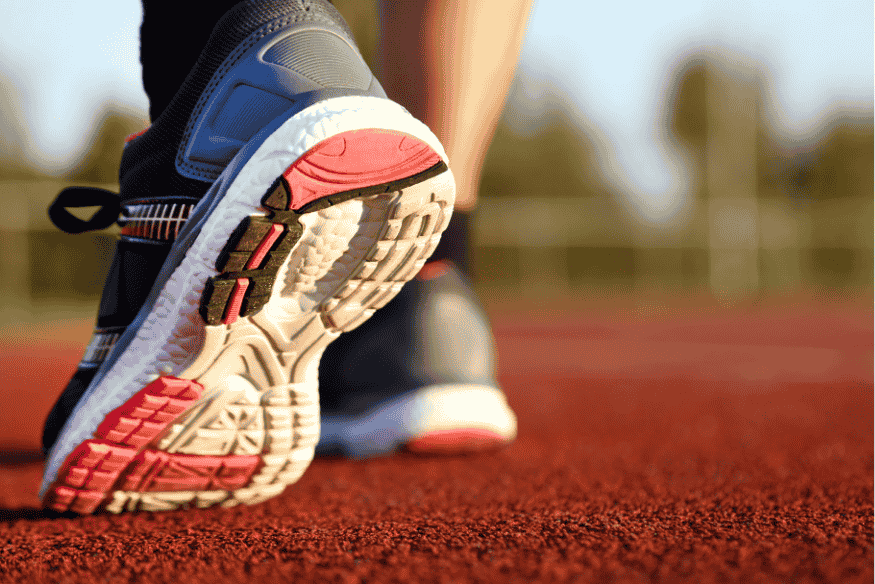 Solado de tênis de corrida com amortecimento visível, em pista esportiva ao pôr do sol.