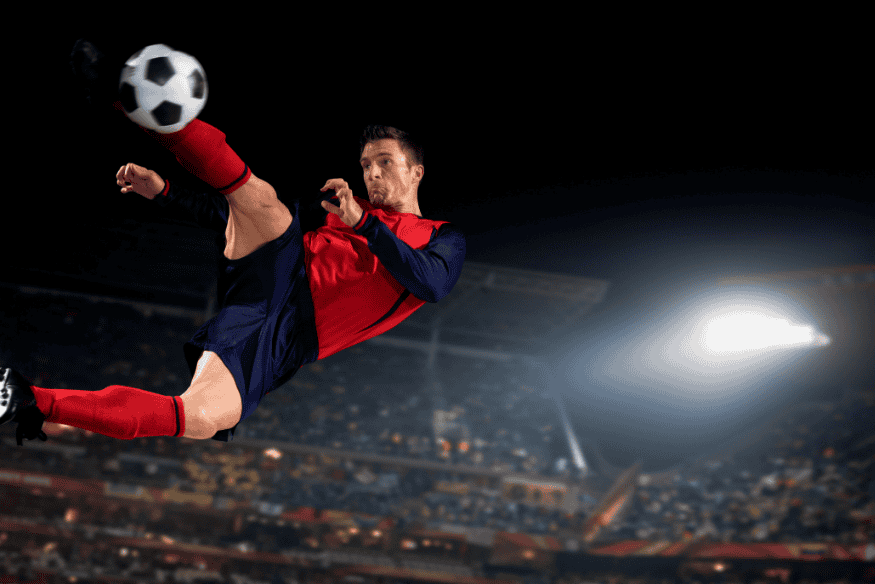 Jogador executando uma bicicleta em partida noturna de futebol