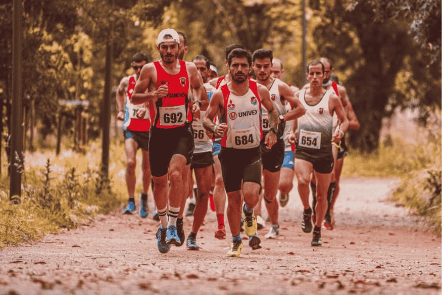 Grupo de corredores participando de prova de corrida em trilha arborizada.