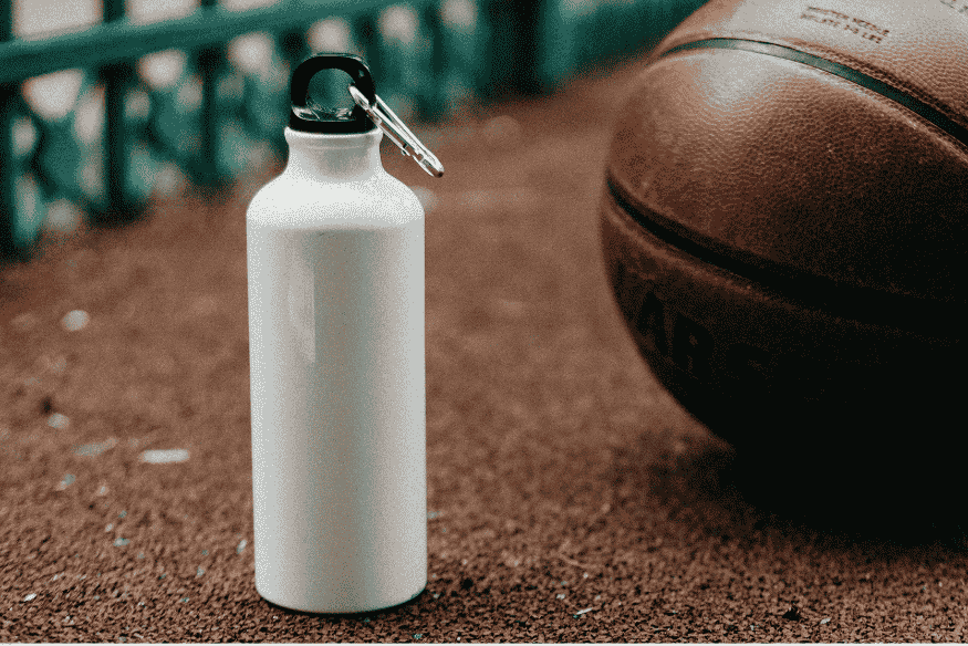 Garrafa reutilizável e bola de basquete sobre a quadra, representando itens básicos para a prática esportiva.