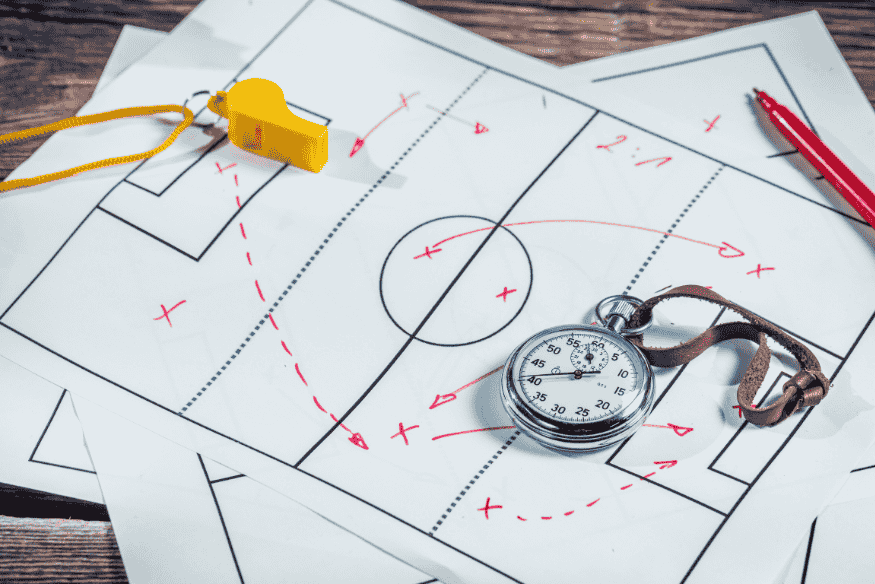 Prancheta com esquema tático de futebol, apito e cronômetro sobre a mesa.