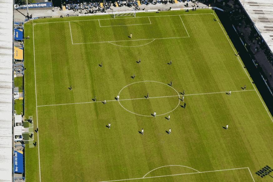 Vista aérea de jogadores posicionados em campo para início de partida de futebol.