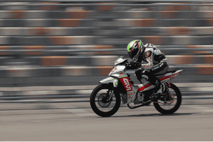 Piloto competindo com moto leve em pista urbana com capacete verde.