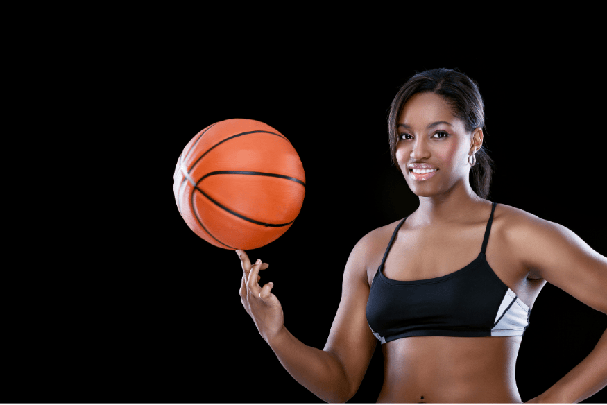Mulher sorridente girando uma bola de basquete no dedo diante de fundo preto.