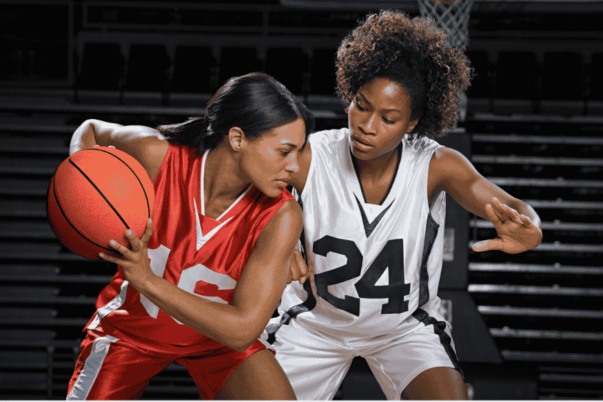 Duas jogadoras em ação durante jogo de basquete, com uma tentando marcar a outra.