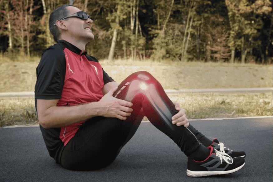 Homem com expressão de dor segurando o joelho com destaque em vermelho, sentado após corrida.