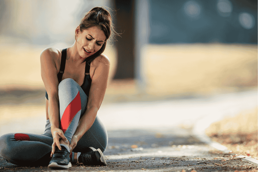 Mulher sentada no chão segurando o tornozelo com expressão de dor após corrida.