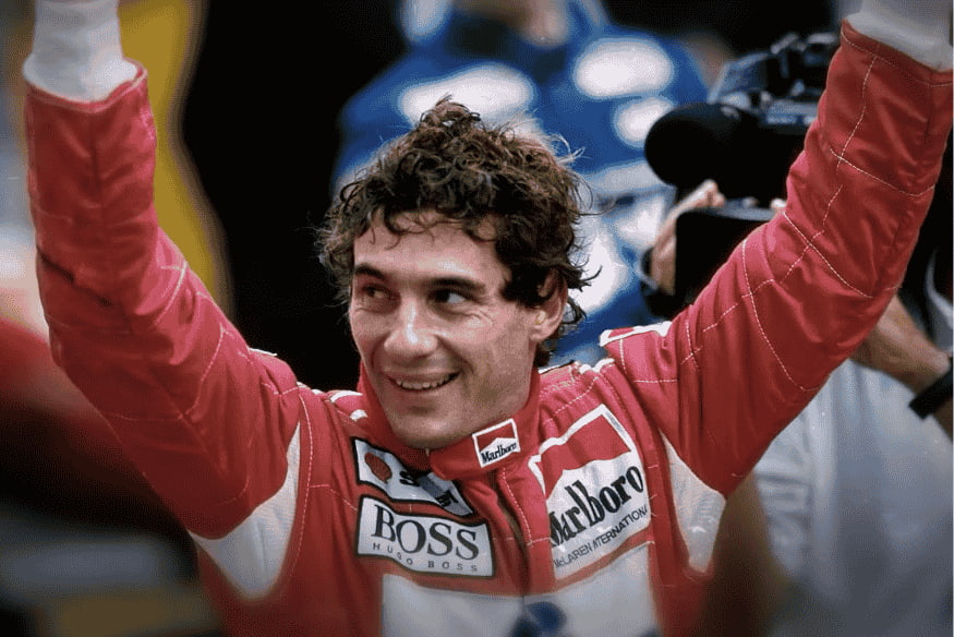 Ayrton Senna sorrindo com os braços erguidos após vencer uma corrida.