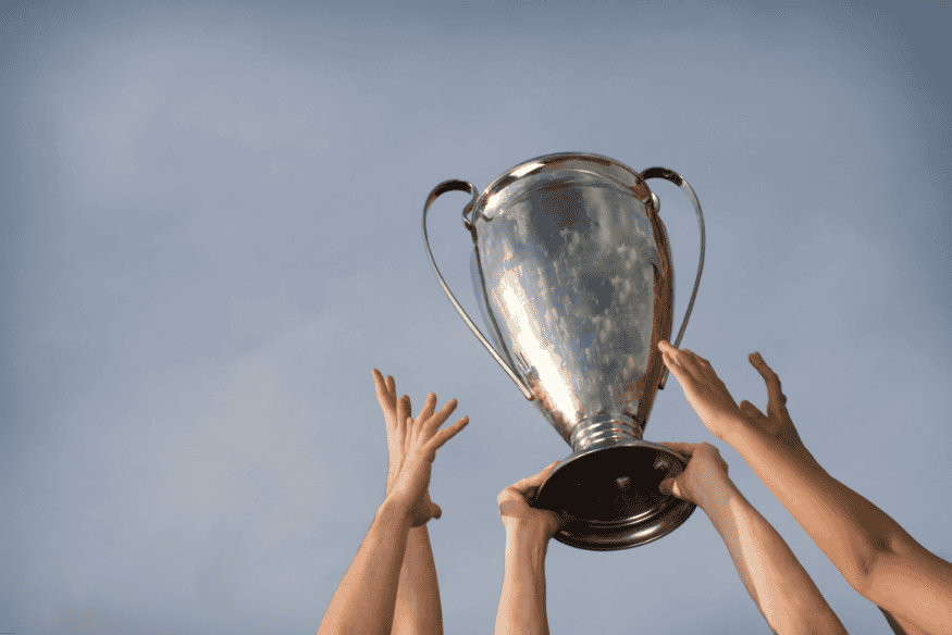 Mãos de jogadores erguendo uma taça de campeonato contra o céu azul