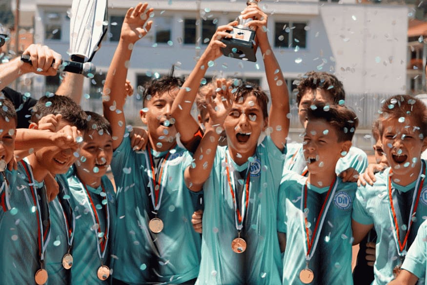 Crianças comemorando vitória com medalhas e troféu de futebol