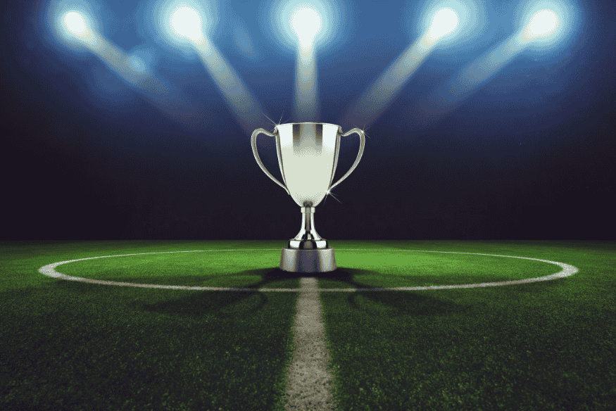 Taça de prata posicionada no centro de um campo de futebol iluminado