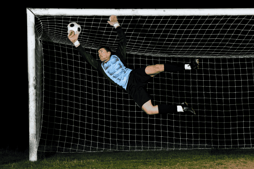 Goleiro voando para defender bola no ângulo.