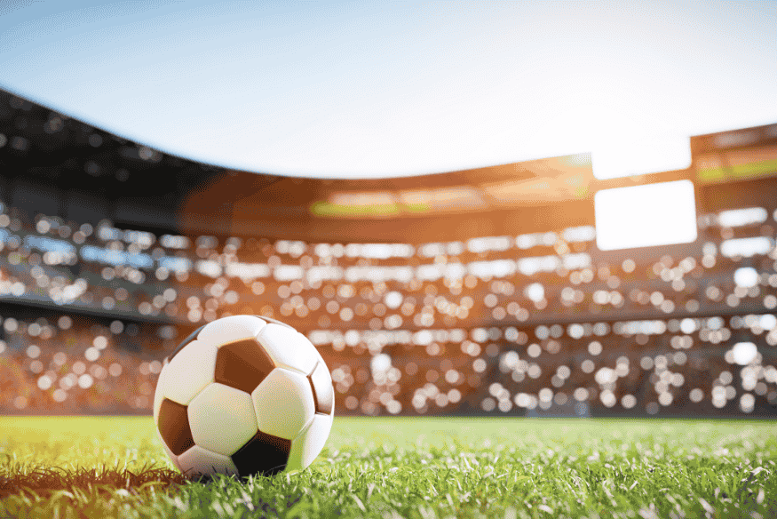 Bola de futebol posicionada no centro de campo em estádio vazio ao entardecer