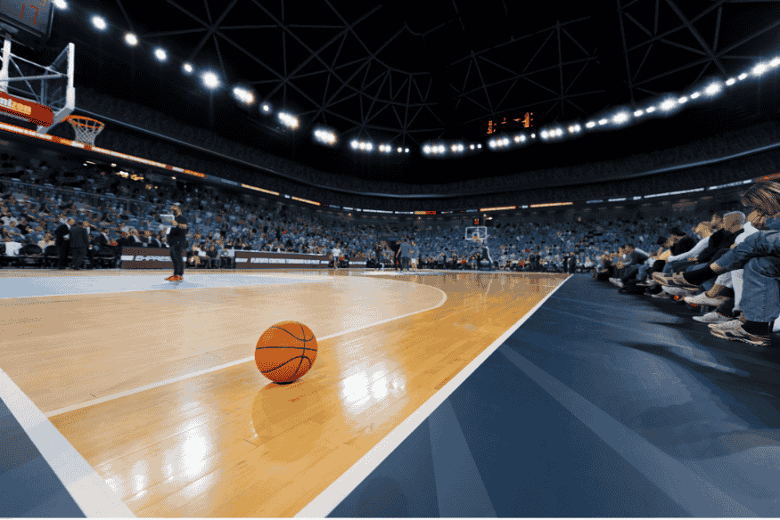 Quadra de basquete com bola no chão e torcida ao fundo durante grande evento esportivo.