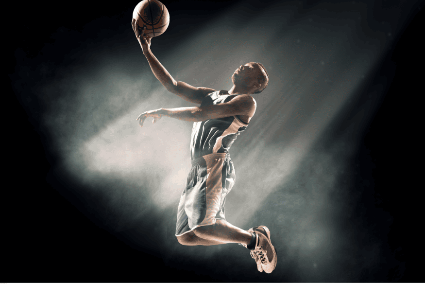 Jogador de basquete em salto, finalizando bandeja em meio a efeito de luz dramático.