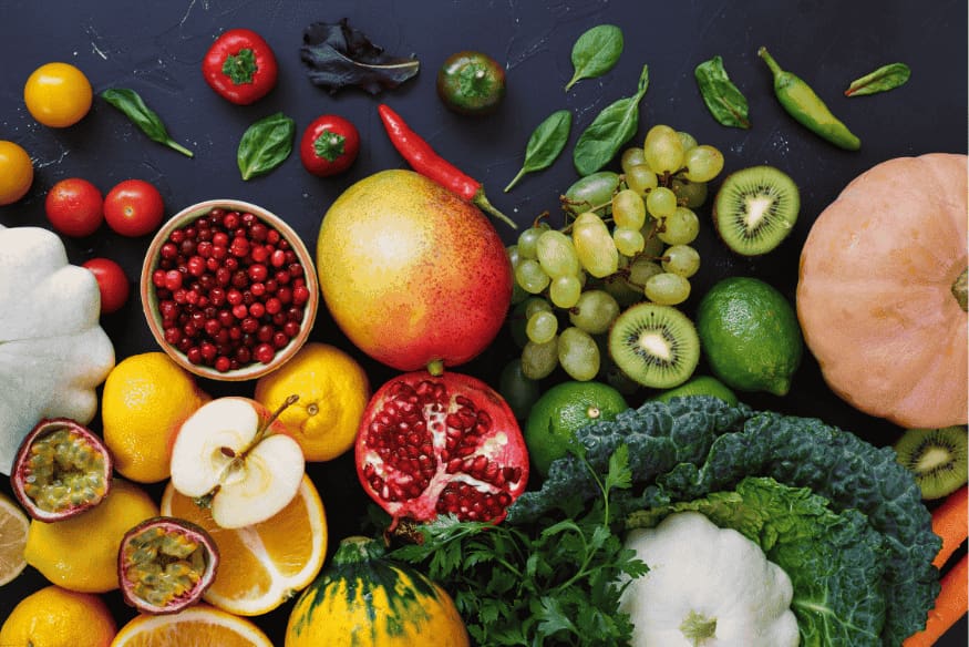 Mesa com frutas, legumes e vegetais frescos de diversas cores sobre fundo escuro.