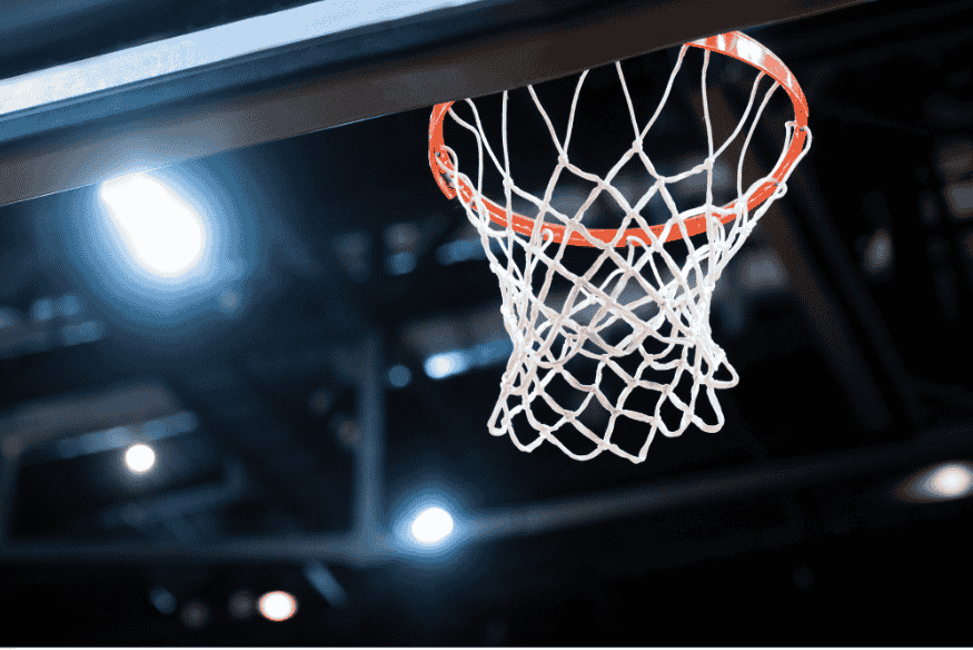 Aro de basquete iluminado visto de baixo, com rede branca destacada.