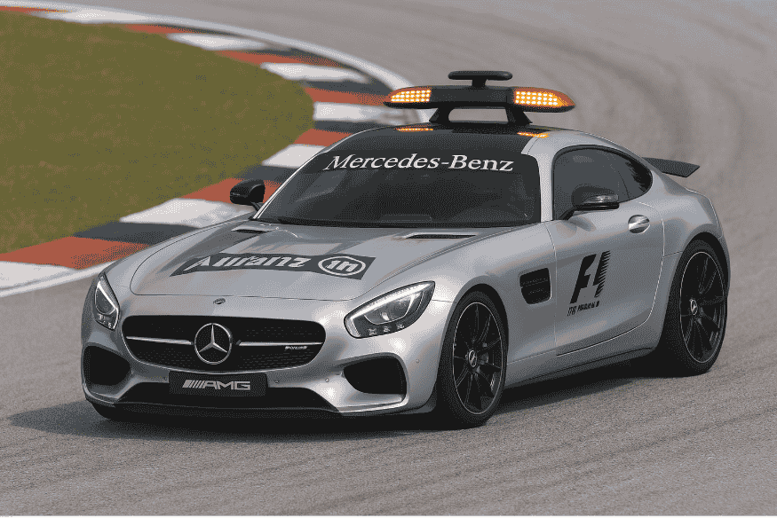 Safety Car antigo na frente de carros de Fórmula 1 em circuito com fumaça no fundo.