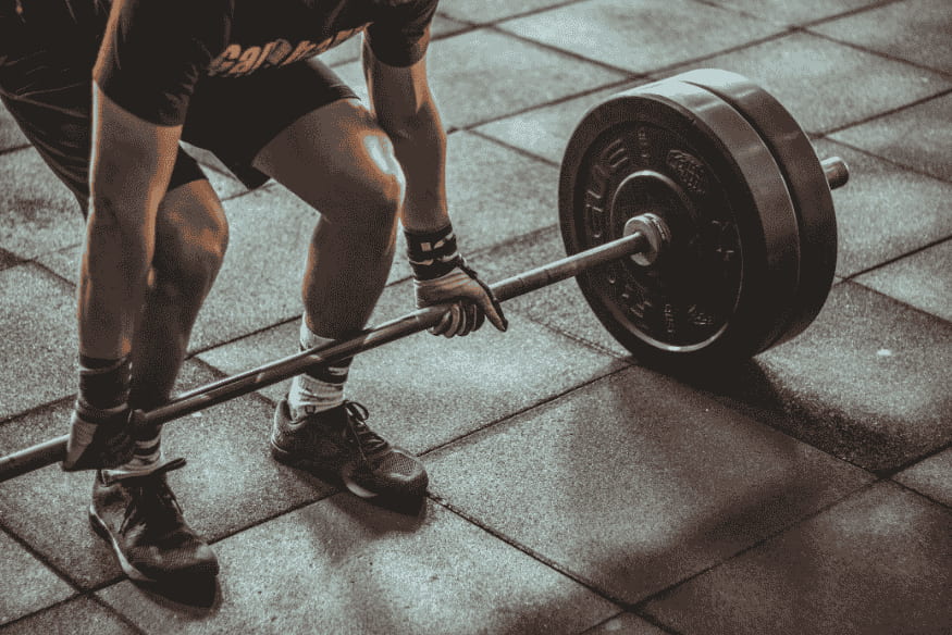 Atleta se preparando para levantar barra com pesos em ambiente de academia