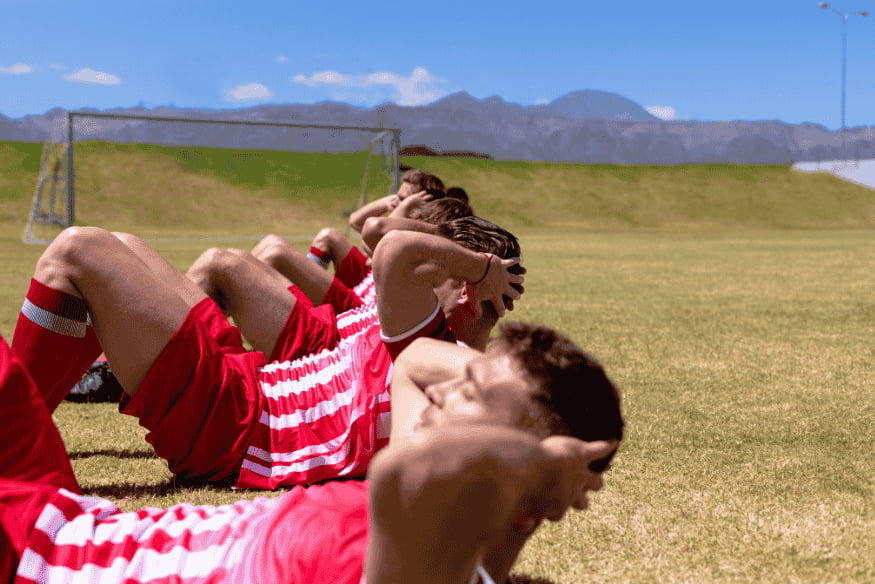 Jogadores de futebol deitados no campo realizando abdominal em série