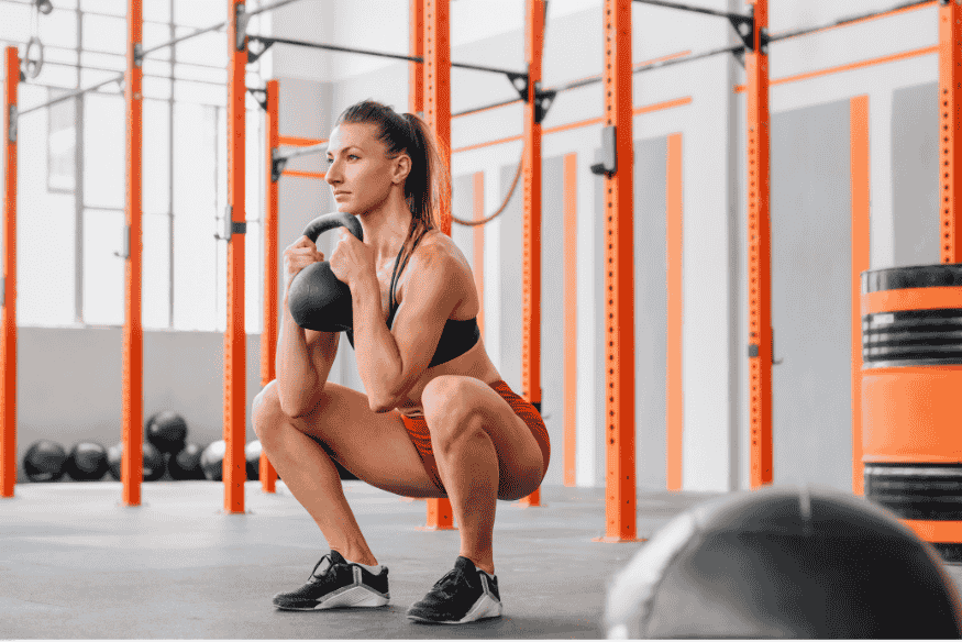 Mulher realizando agachamento com kettlebell em academia de cross training.