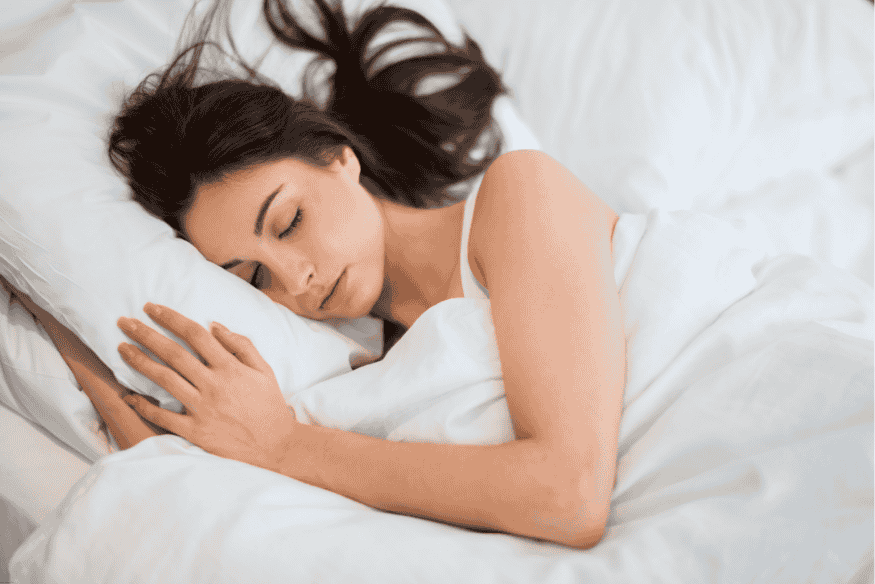 Mulher dormindo profundamente em cama com lençóis brancos, em ambiente calmo e escuro.