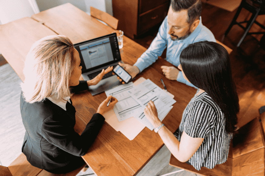 Três pessoas reunidas analisando documentos financeiros e propostas de negociação, representando a decisão entre acordo parcelado e quitação à vista para sair do negativo.