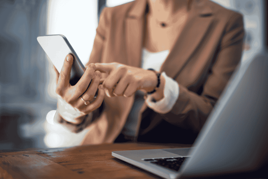 Mulher utilizando smartphone ao lado de notebook, simbolizando o contato com a empresa credora para regularizar a situação após quitação da dívida.