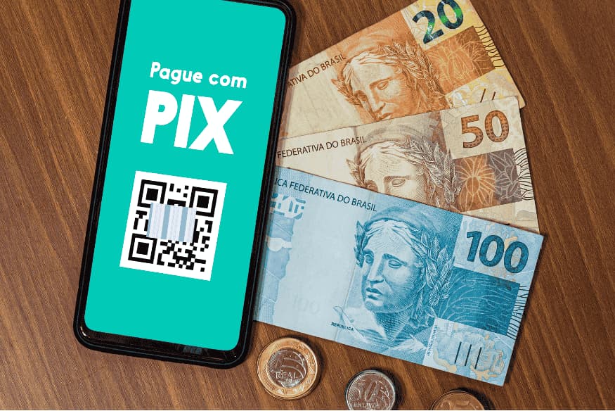Celular com QR Code do Pix ao lado de notas de real, ilustrando o Pix como opção de pagamento no Brasil