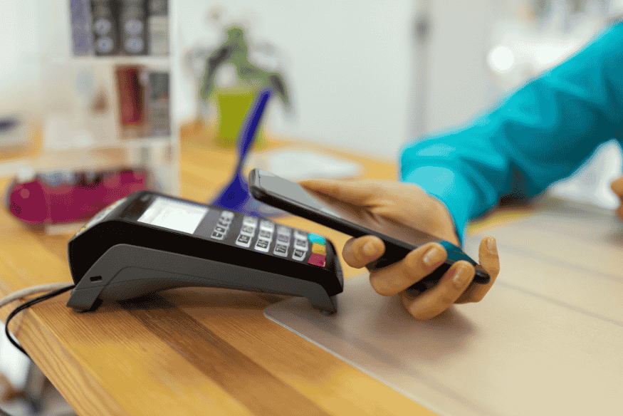 Smartphone sendo usado para pagamento por aproximação em terminal, mostrando uma alternativa moderna ao cartão físico.